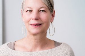Picture of older woman with hoop earrings smiling to partially reveal her upper teeth