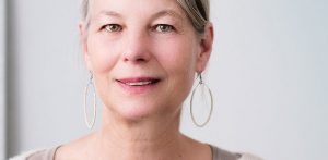 Picture of older woman with hoop earrings smiling to partially reveal her upper teeth