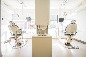 Two sleek white dental chairs facing wall to floor window on a bright day