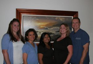 Photograph of Dr. Stockdale and four team members standing in front of a portrait of waves crashing on a beach