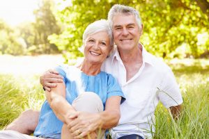 Smiling older couple sitting in a grassy field with trees in the background