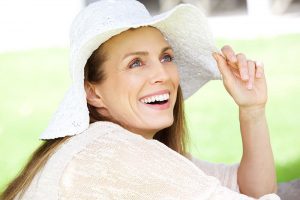 Smiling blue-eyed, blonde woman outdoors wearing white hat and white top